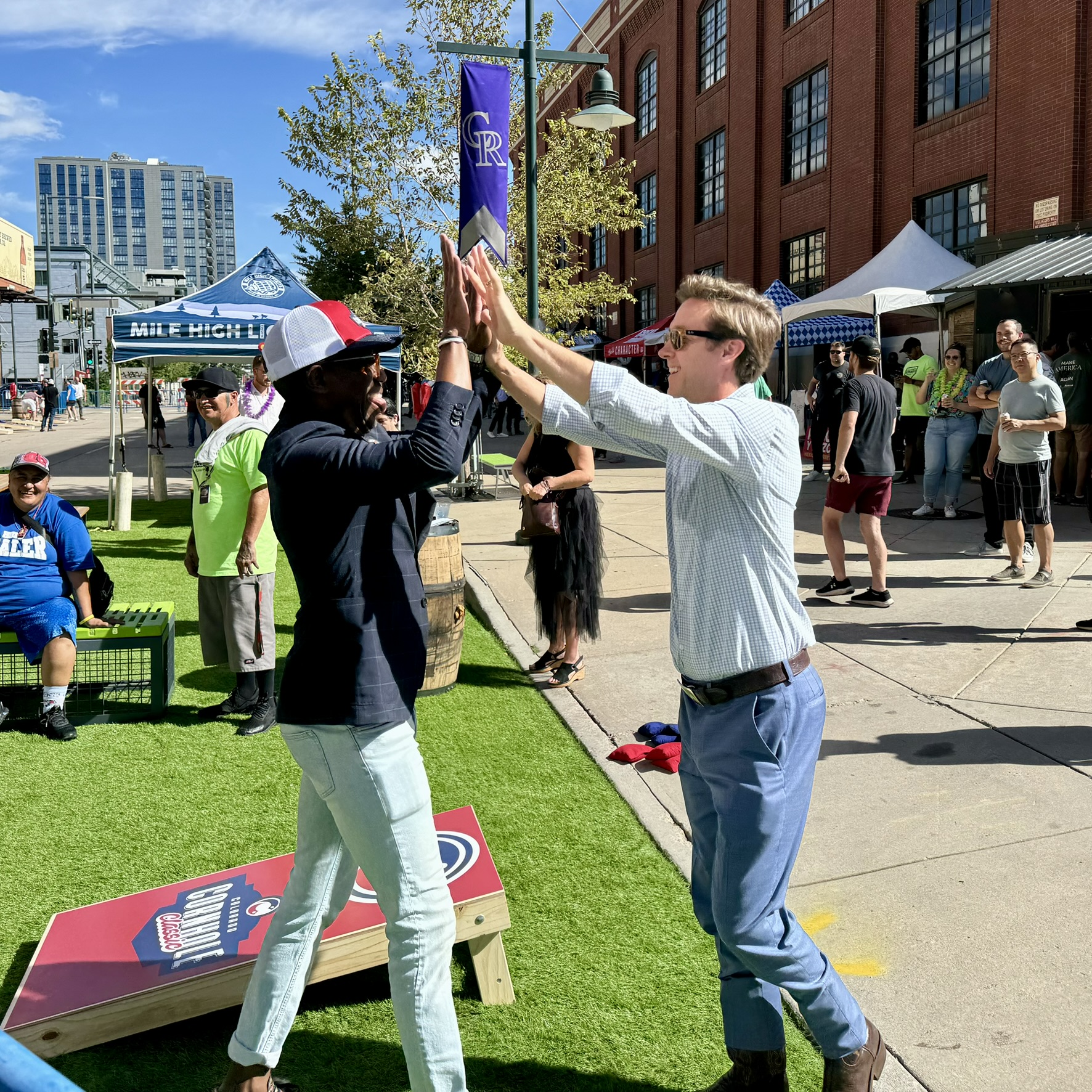 High five over a Rockies Cornhole Classic board at the Ballpark District festival
